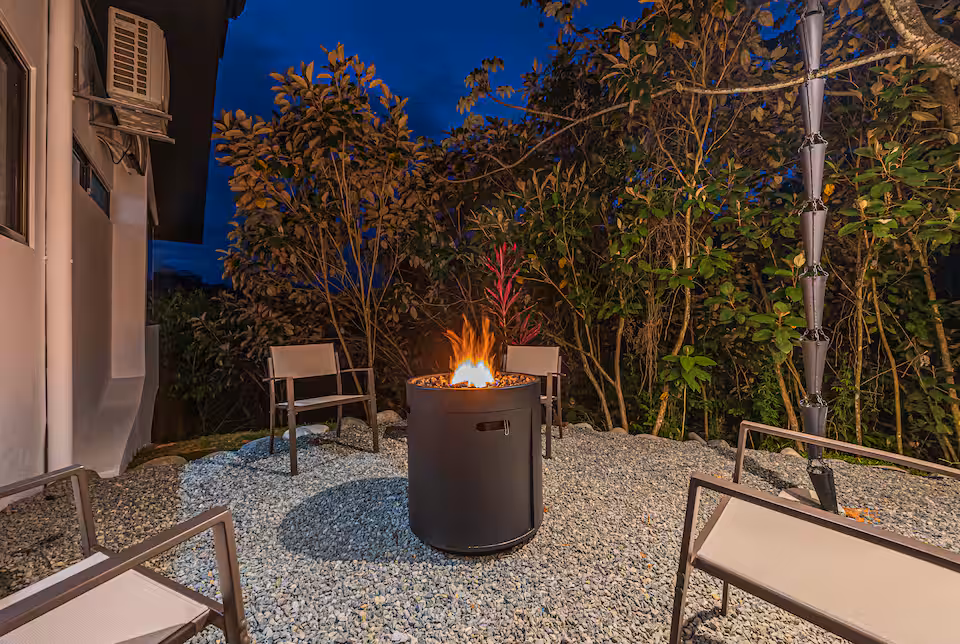Lit gas fire pit ringed by chairs on a gravel terrace at night at KsaLinda villa, Costa Rica